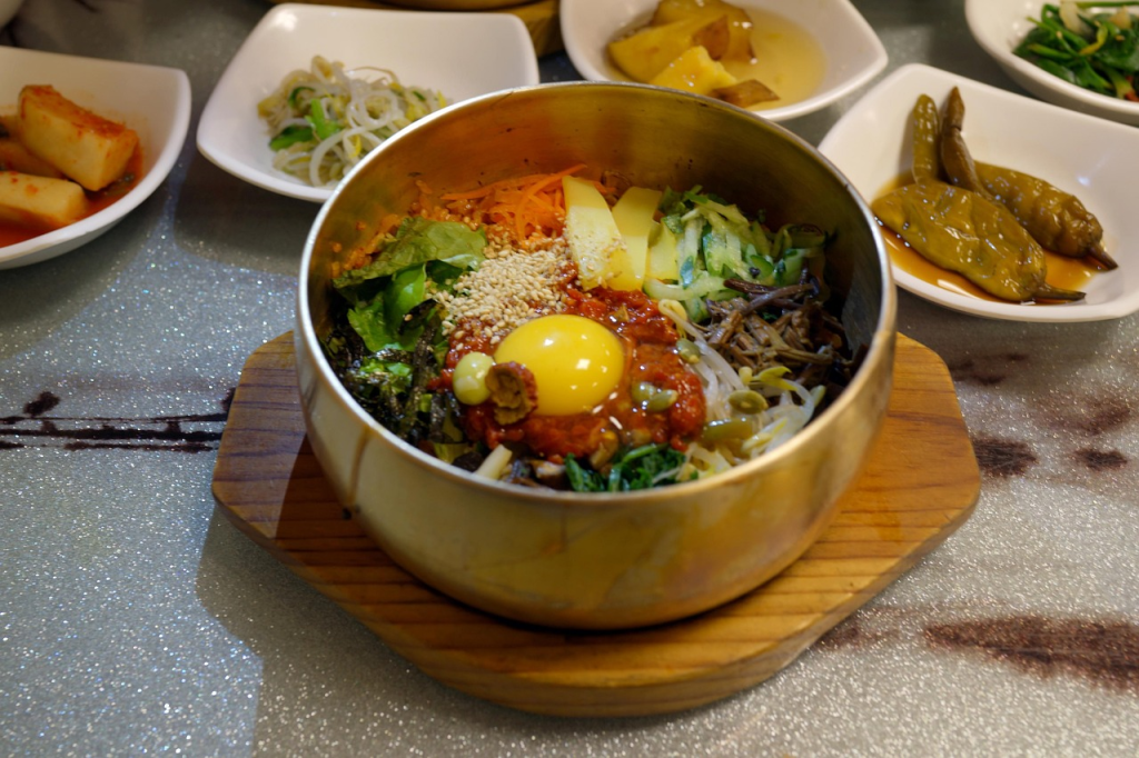 Jeonju Bibimbap served with fresh vegetables, beef, gochujang, and egg yolk in a brass bowl