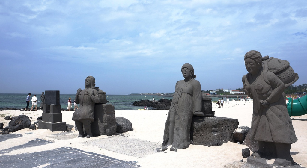 Stone statues of haenyeo female divers and dol hareubang on a beach in Jeju Island, South Korea