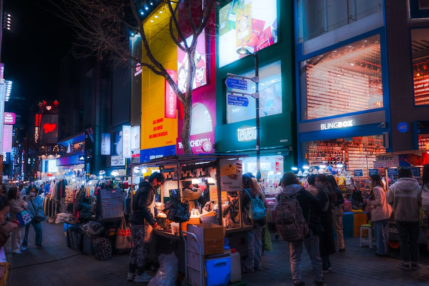 Myeongdong shopping street in Seoul with neon lights, street food stalls, and crowds of travelers