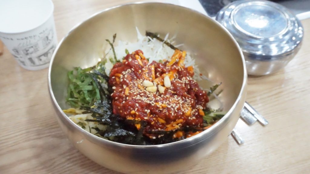 A bowl of yukhoe bibimbap topped with seasoned raw beef, shredded vegetables, seaweed, and sesame seeds.