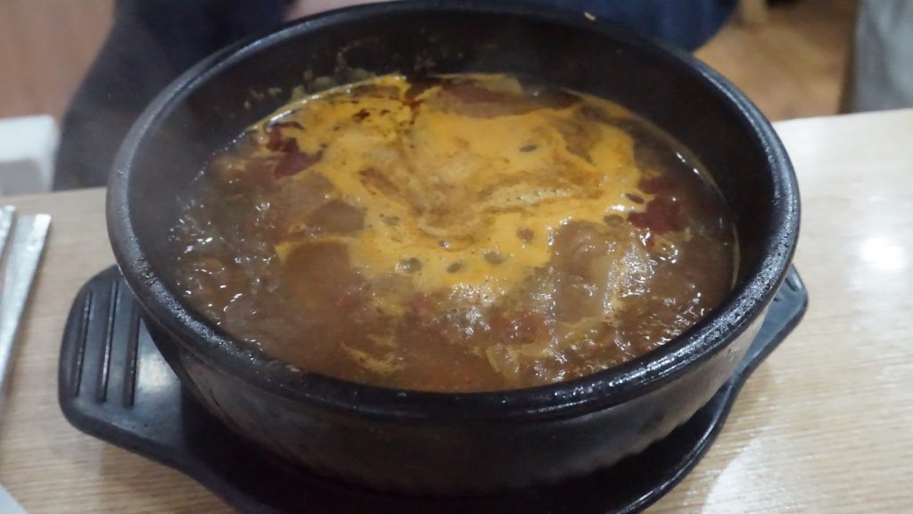 A steaming bowl of seonji soup in a black pot, with rich broth bubbling on the surface.