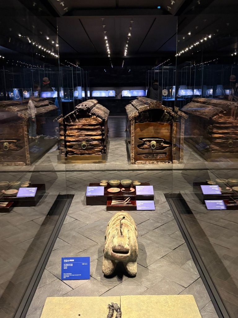 Dark exhibition gallery at National Gongju Museum with large tomb-related displays and artifacts under spotlights.